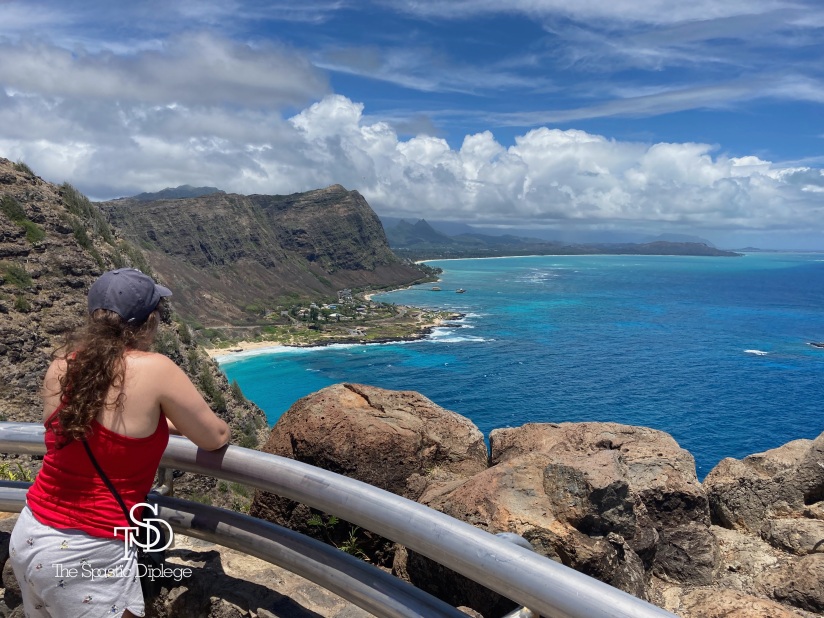 Myself, standing with my back to the camera. I am overlooking a beautiful view at the end of a hike in Honolulu, Hawaii. The view includes a beautiful blue ocean and a rocky shoreline.